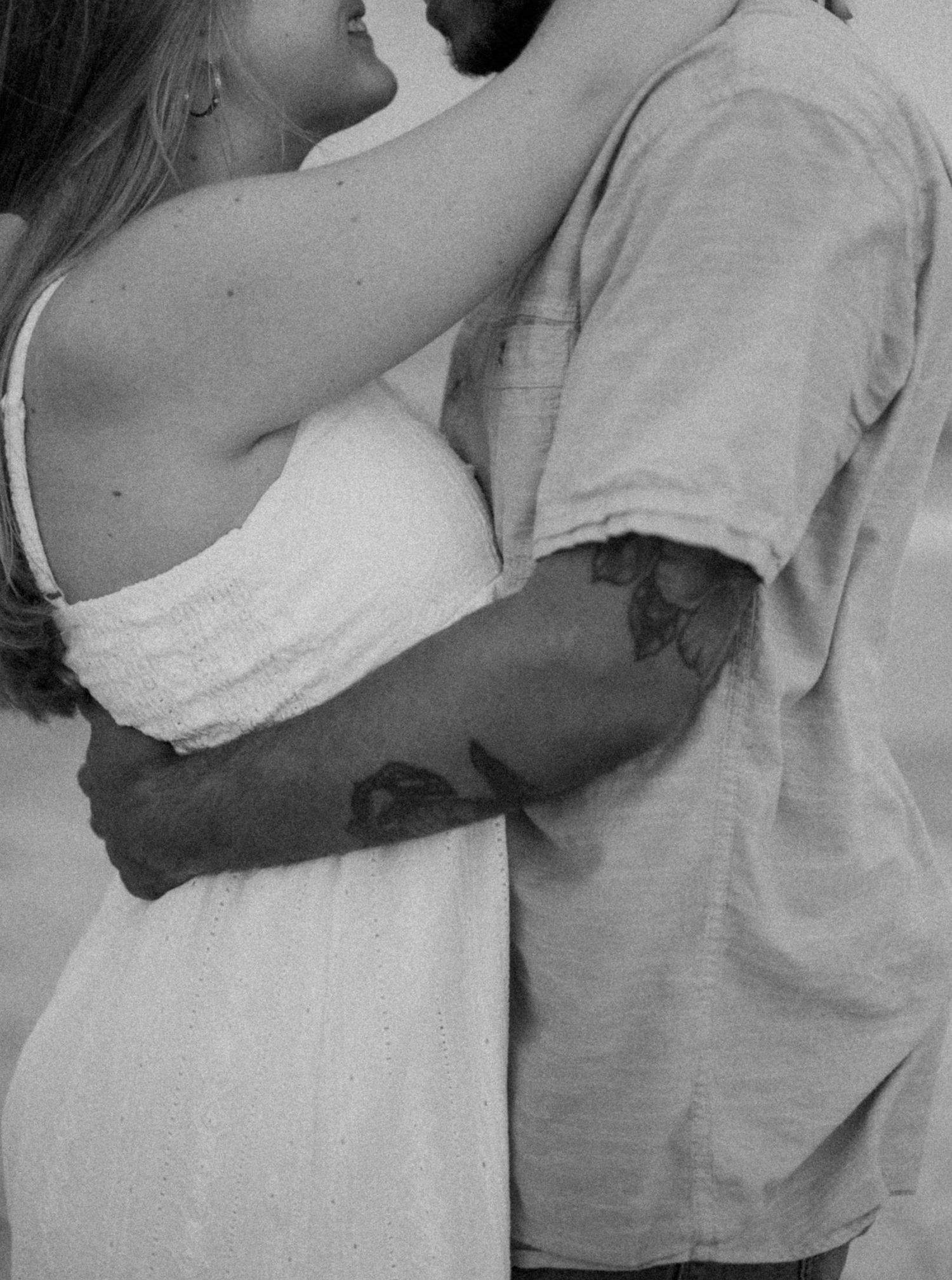 Black and white romantic portrait of a couple embracing in casual attire.