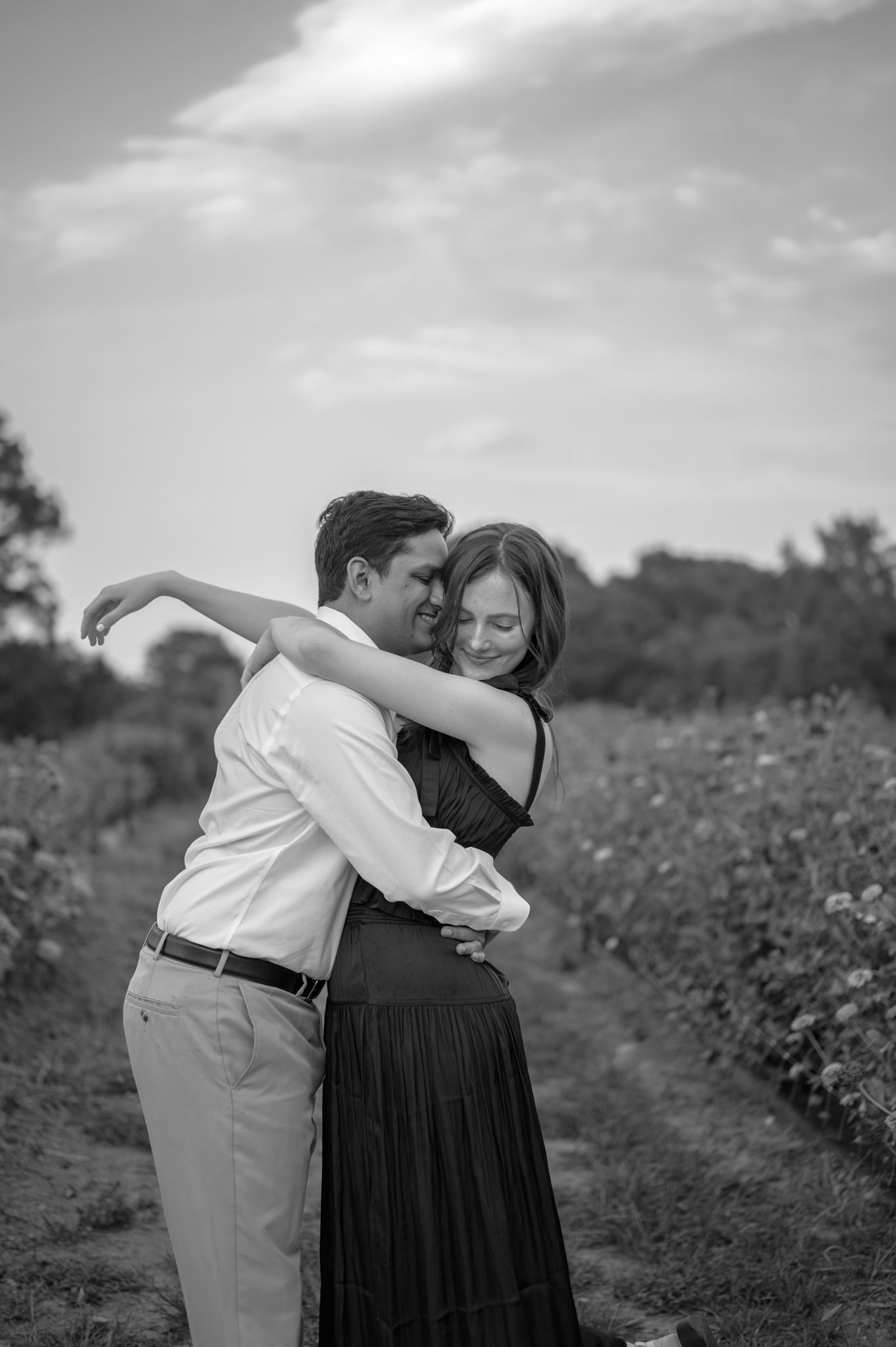 A black and white photo of a couple dancing in a field on a cloudy day.