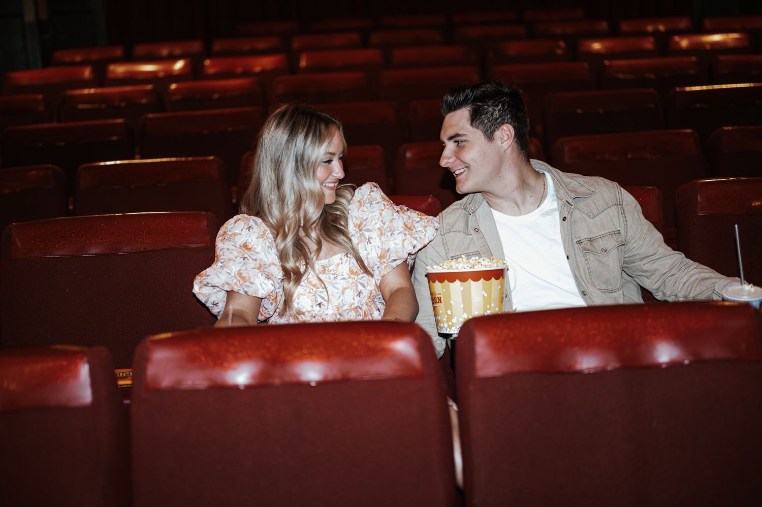 A couple enjoying a movie date while sitting in red theater seats with popcorn.