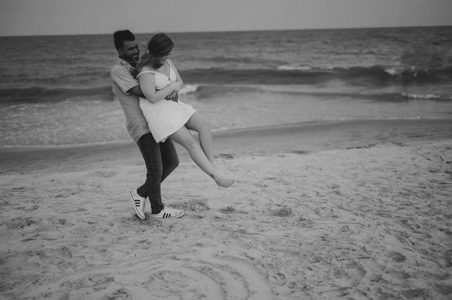 Black and white beach scene with couple sharing intimate moments by the ocean.