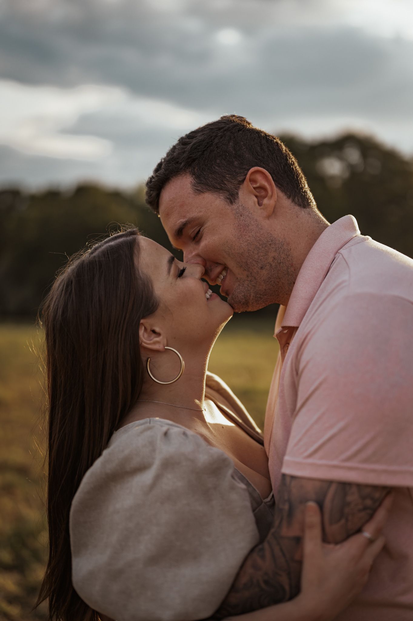 Couple sharing romantic kisses in a golden-lit field at sunset.