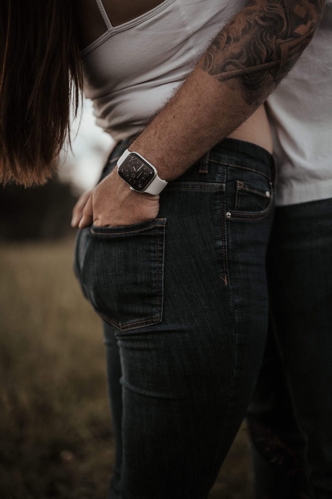 Intimate couple in casual attire embracing against blurred outdoor background.