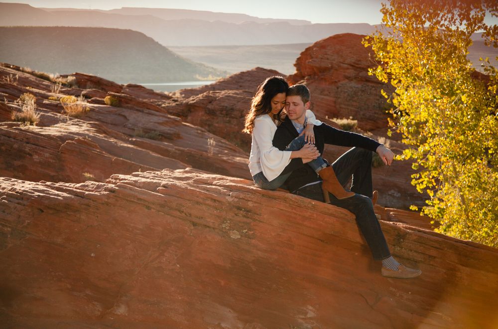 Couple sitting together on red sandstone rocks at sunset with canyon and lake views behind them.