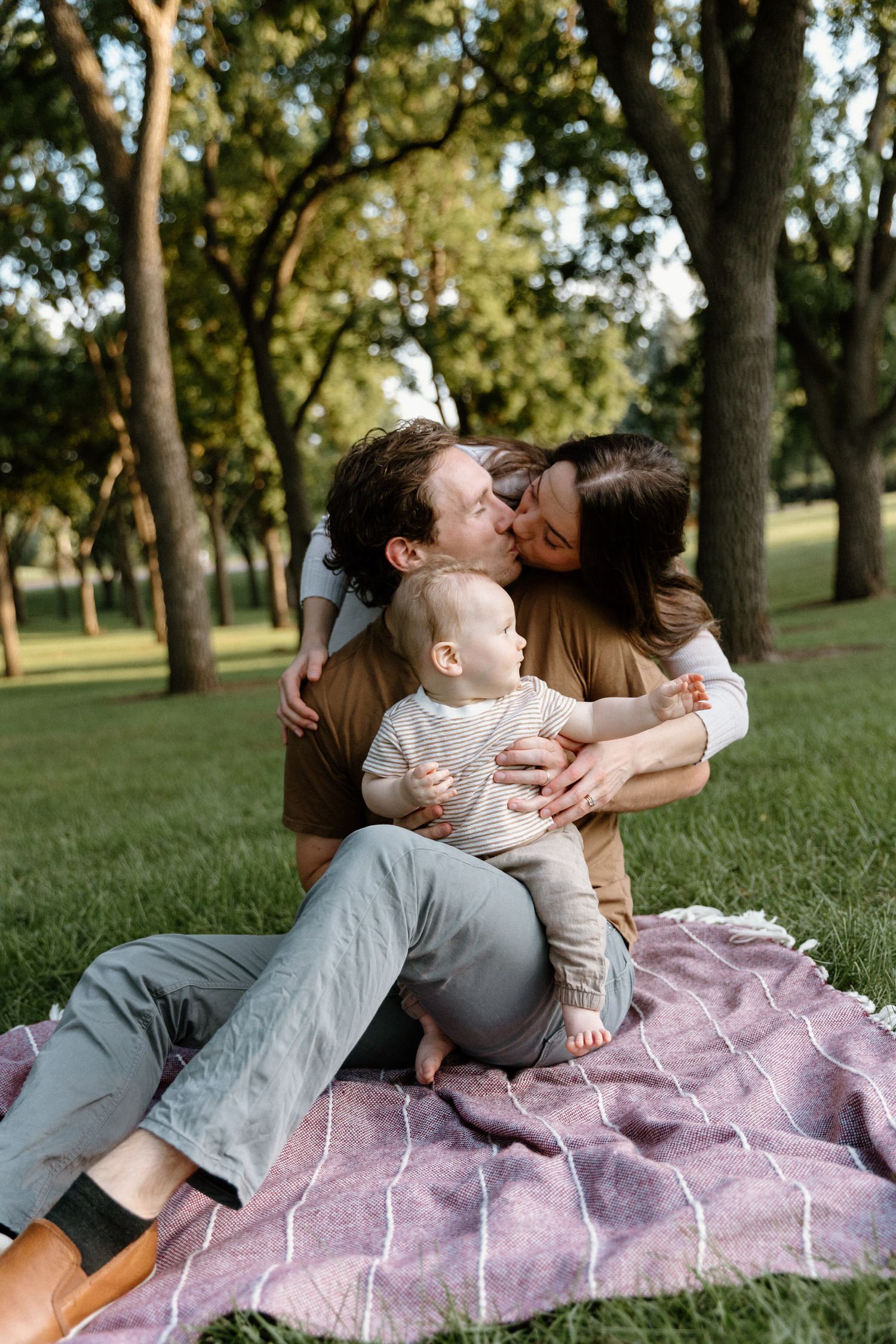 Candid family moments captured on a purple blanket under shady trees.