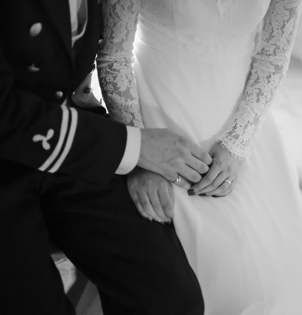 Black and white detail shot of military uniform and wedding dress with hands clasped.