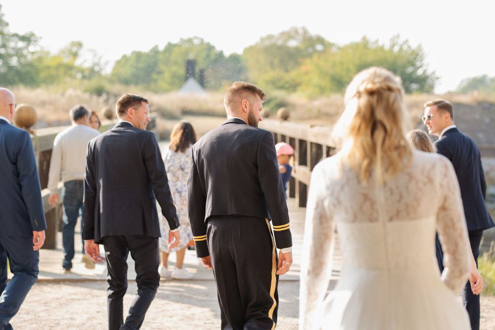 A wedding party walks along a path on a sunny day with the bride in white and others in formal attire.