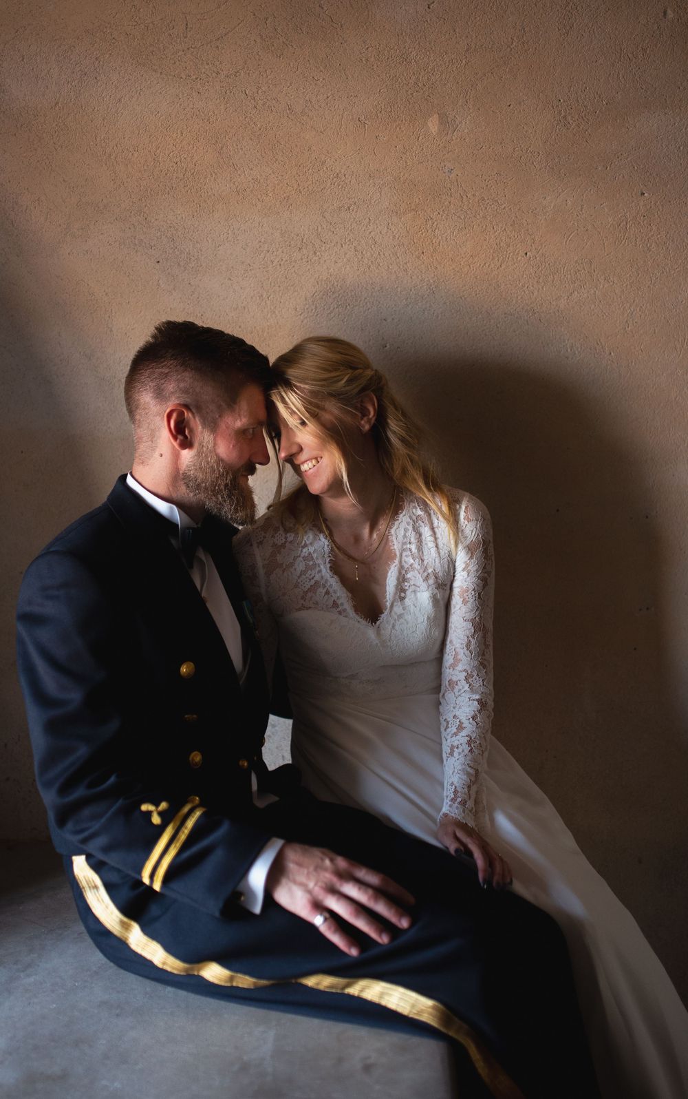 Intimate wedding portrait in moody lighting against textured wall.
