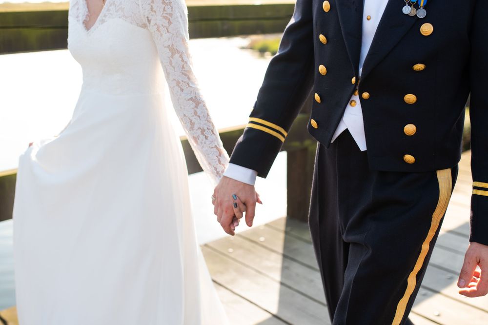 Close-up of clasped hands showing military uniform sleeve and white lace wedding dress details.