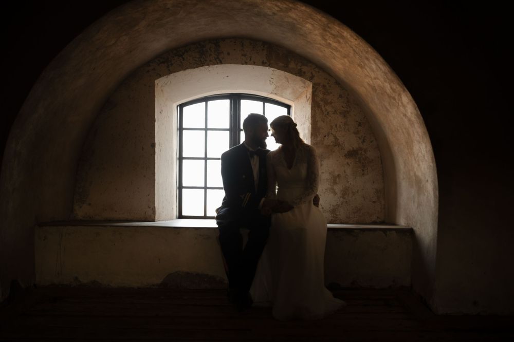 Silhouetted figures in arched stone window create romantic wedding portrait.