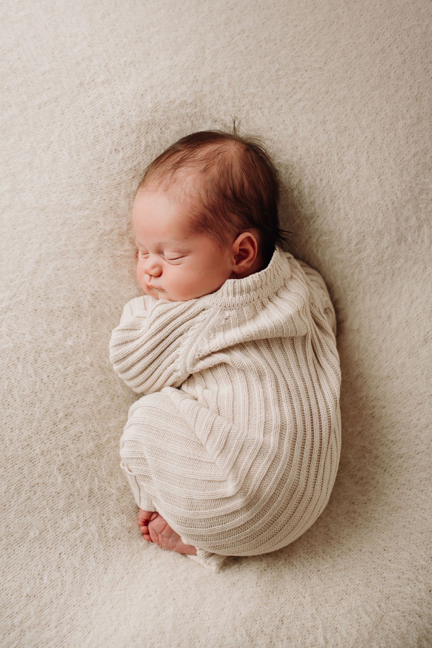 Peaceful newborn baby sleeping while wrapped in a soft white ribbed knit blanket.