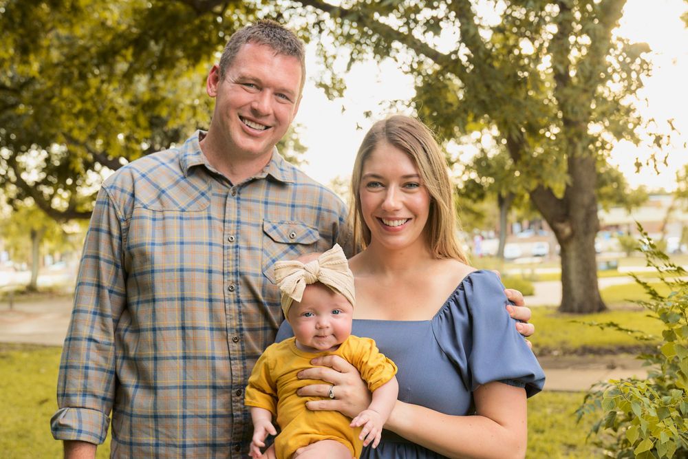 Happy family poses together outdoors on a sunny day in a park setting.