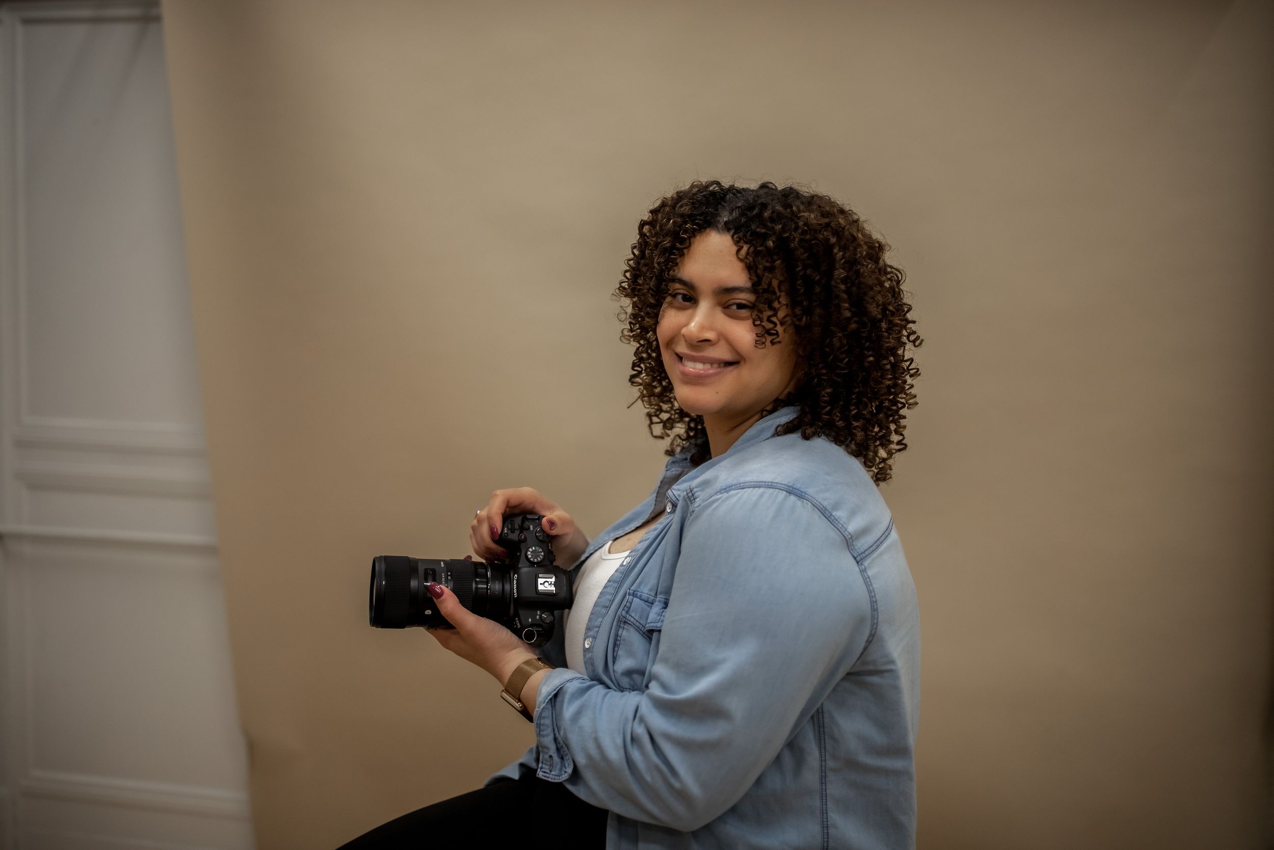 Connecticut based Photographer in denim jacket holding camera in interior setting.