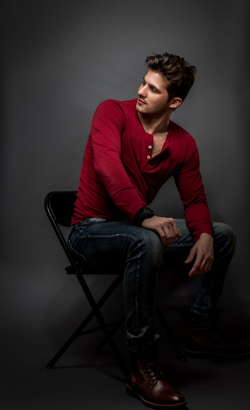 Portrait of model in red henley shirt sitting on chair in dramatic studio lighting.