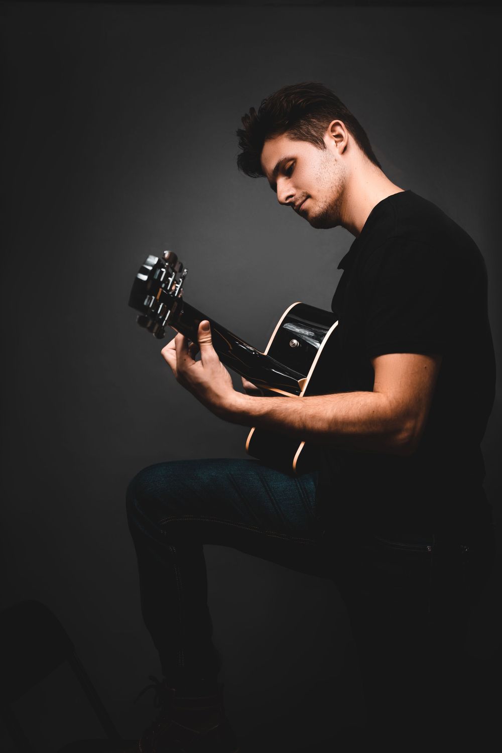 Studio portrait of musician playing acoustic guitar against dark background.