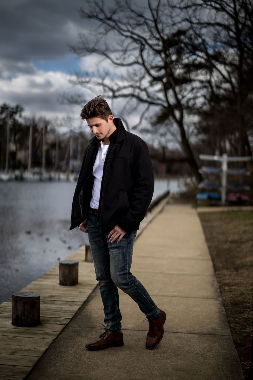 Dramatic outdoor portrait of a person in dark clothing on a waterfront boardwalk.