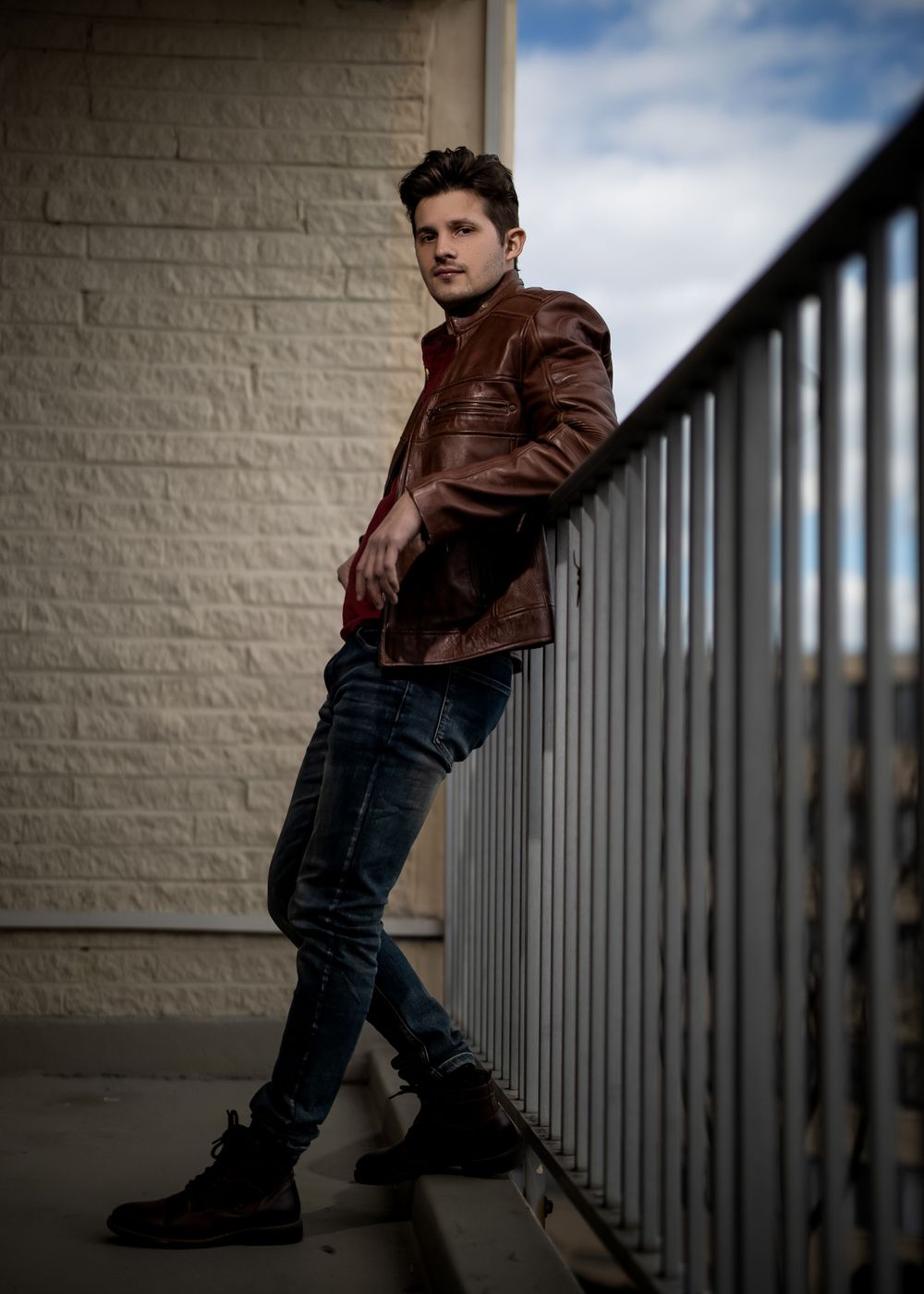 Urban fashion shot of a person in brown leather jacket leaning against railing.