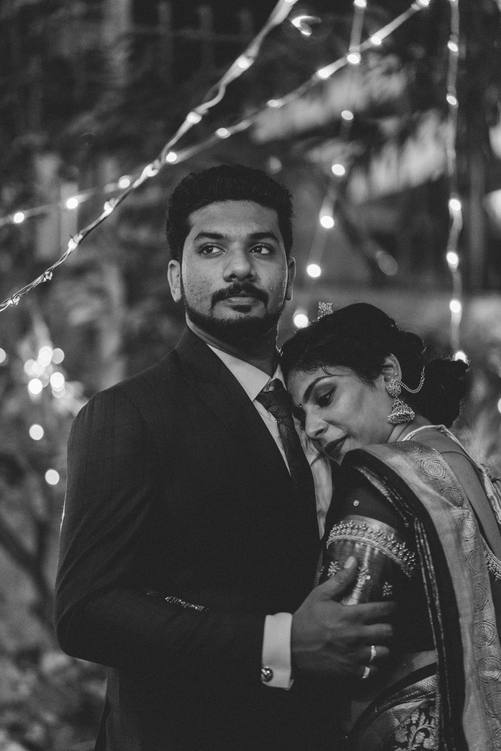 A black and white wedding portrait illuminated by delicate string lights in an outdoor setting.