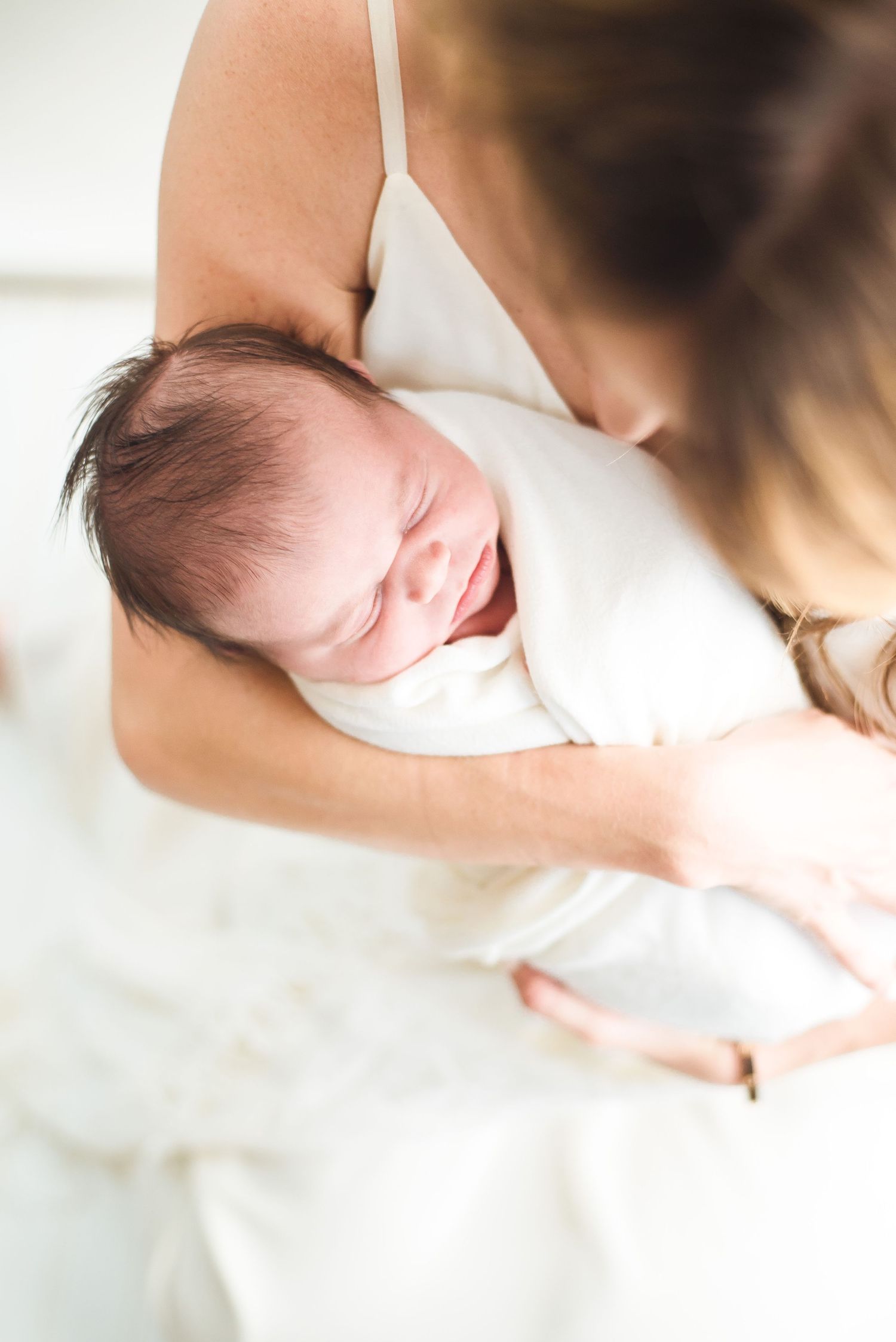 Soft focus intimate portrait of parent cradling newborn baby in natural light.