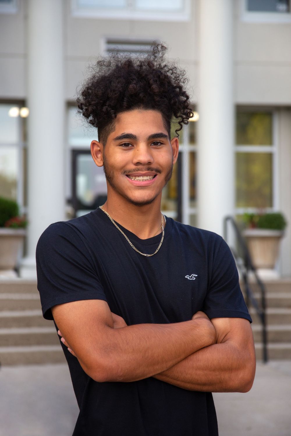 Thomas High School graduate stands with arms crossed in from of his school during his senior photos.