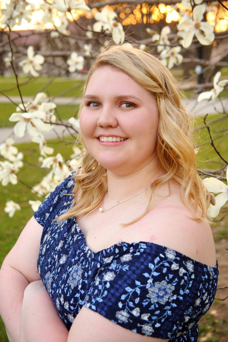 Ohio State University graduate stands in front of white flowers at sunset on the OSU Oval.