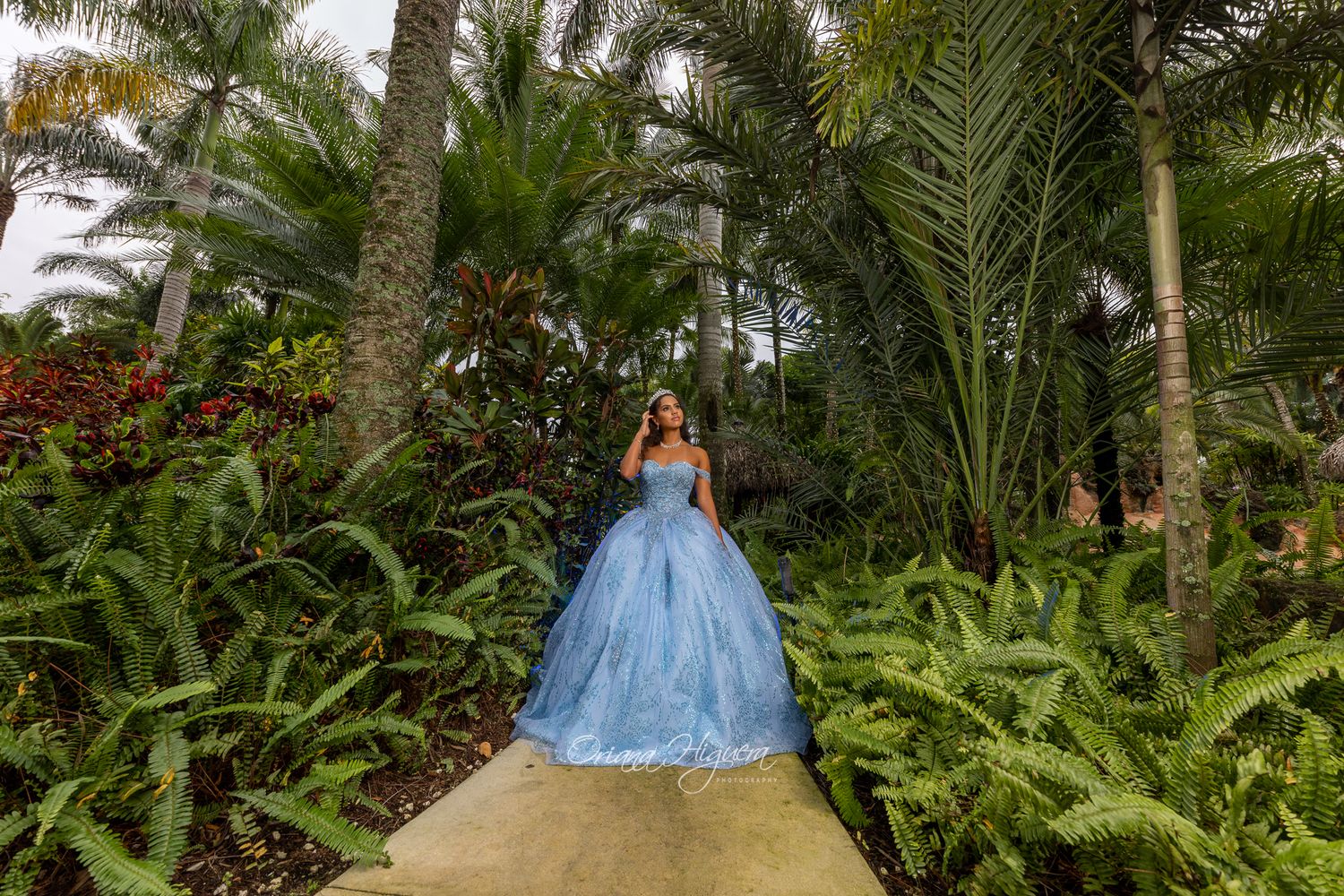 Blue ball gown contrasting against lush tropical garden with palm trees.