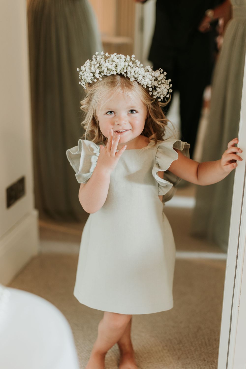 A small figure wearing a white dress and baby's breath crown standing in a hallway.