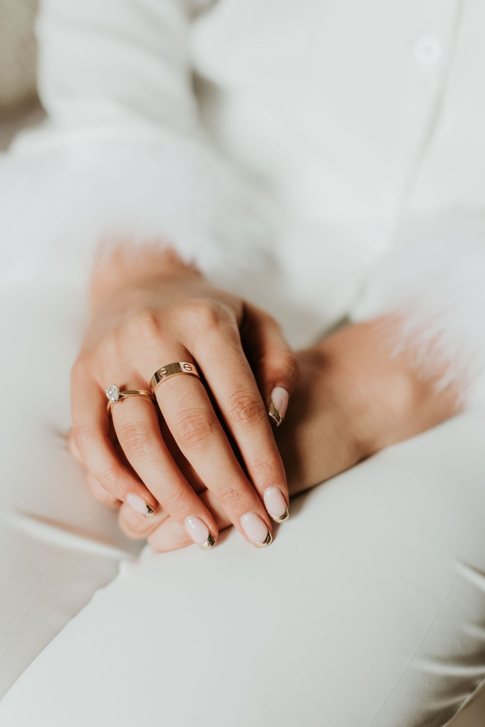 Close-up of manicured hands with wedding rings resting on white fabric.