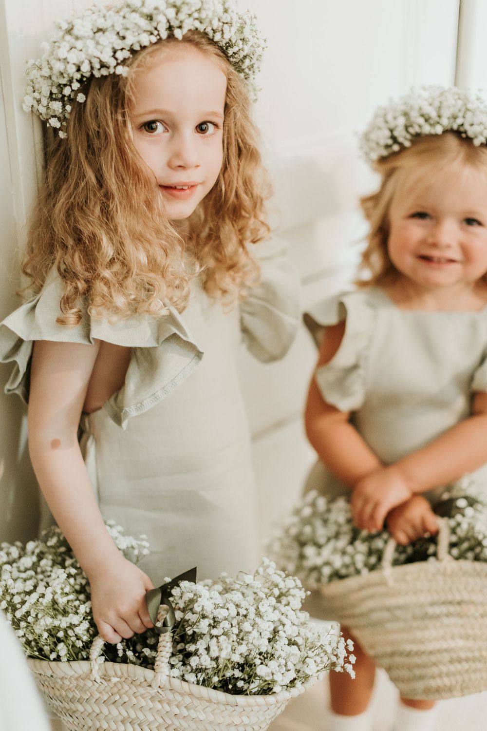 Two small figures in matching white dresses holding baskets of baby's breath flowers.