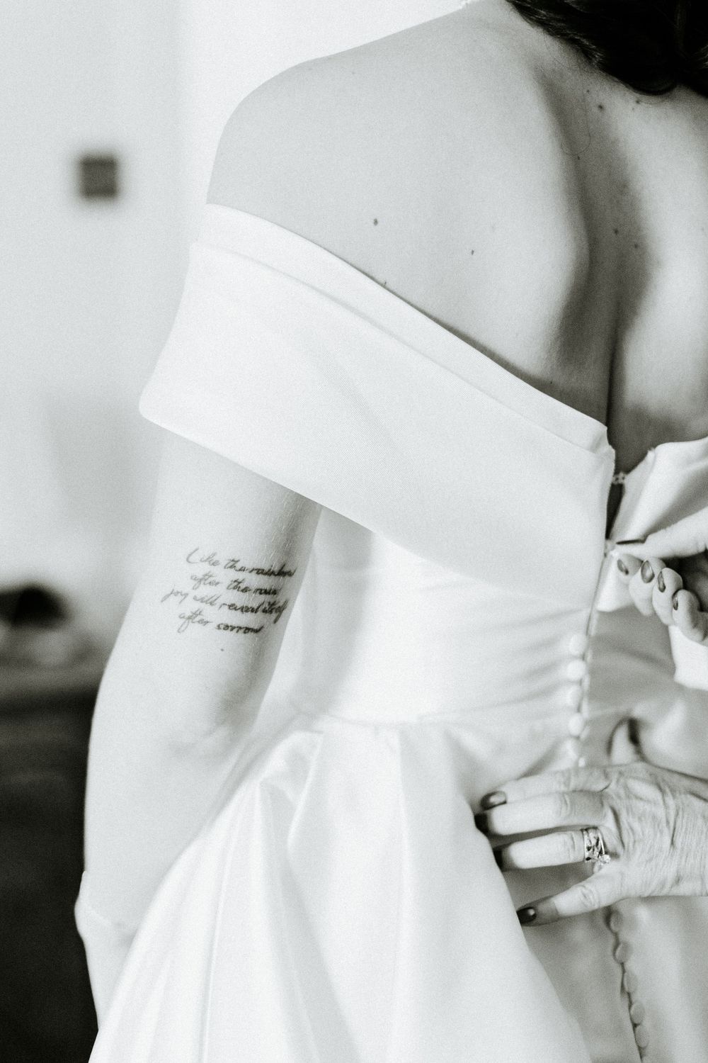 Close-up black and white photo showing details of an off-shoulder wedding dress with text tattoo visible.