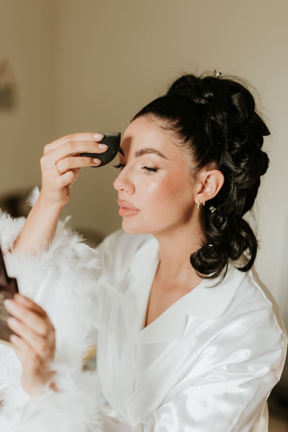Side profile of someone getting makeup applied while wearing a white silk robe.