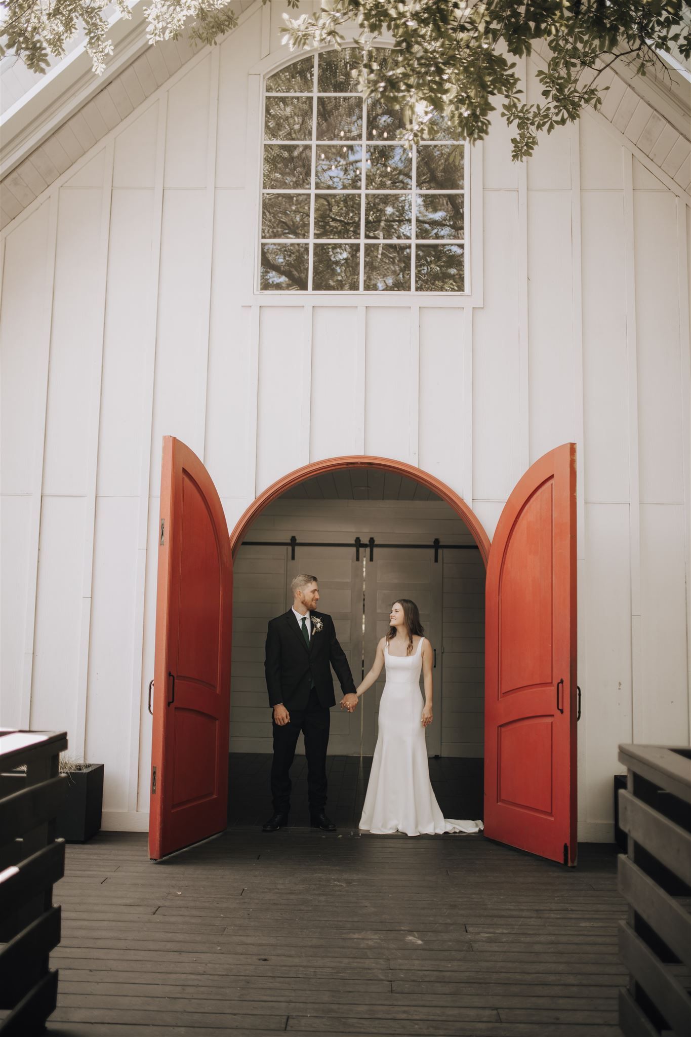 Elegant couple standing in doorway of white chapel with distinctive red doors.