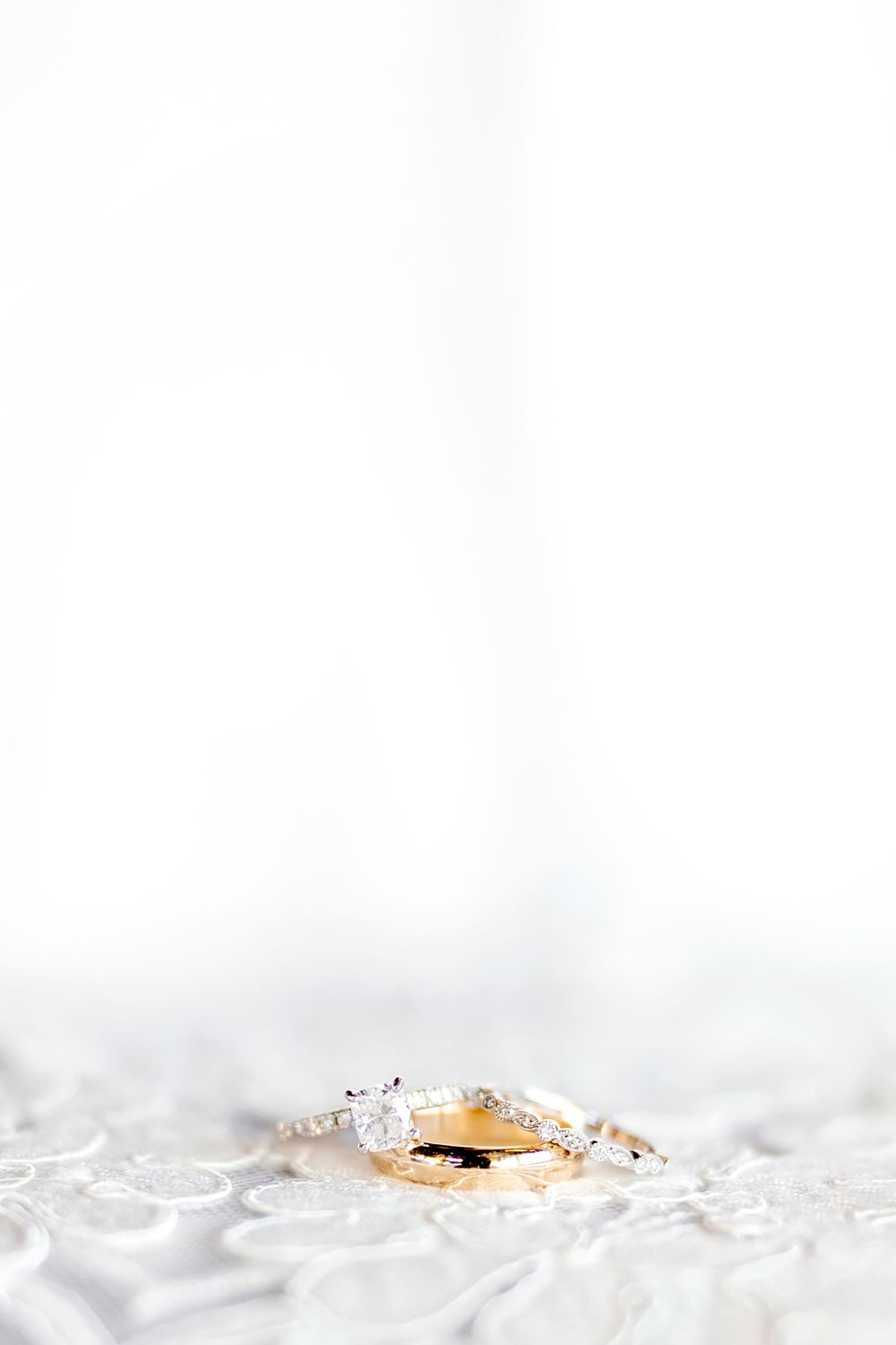 Gold wedding rings nestled in white lace with elegant lighting.