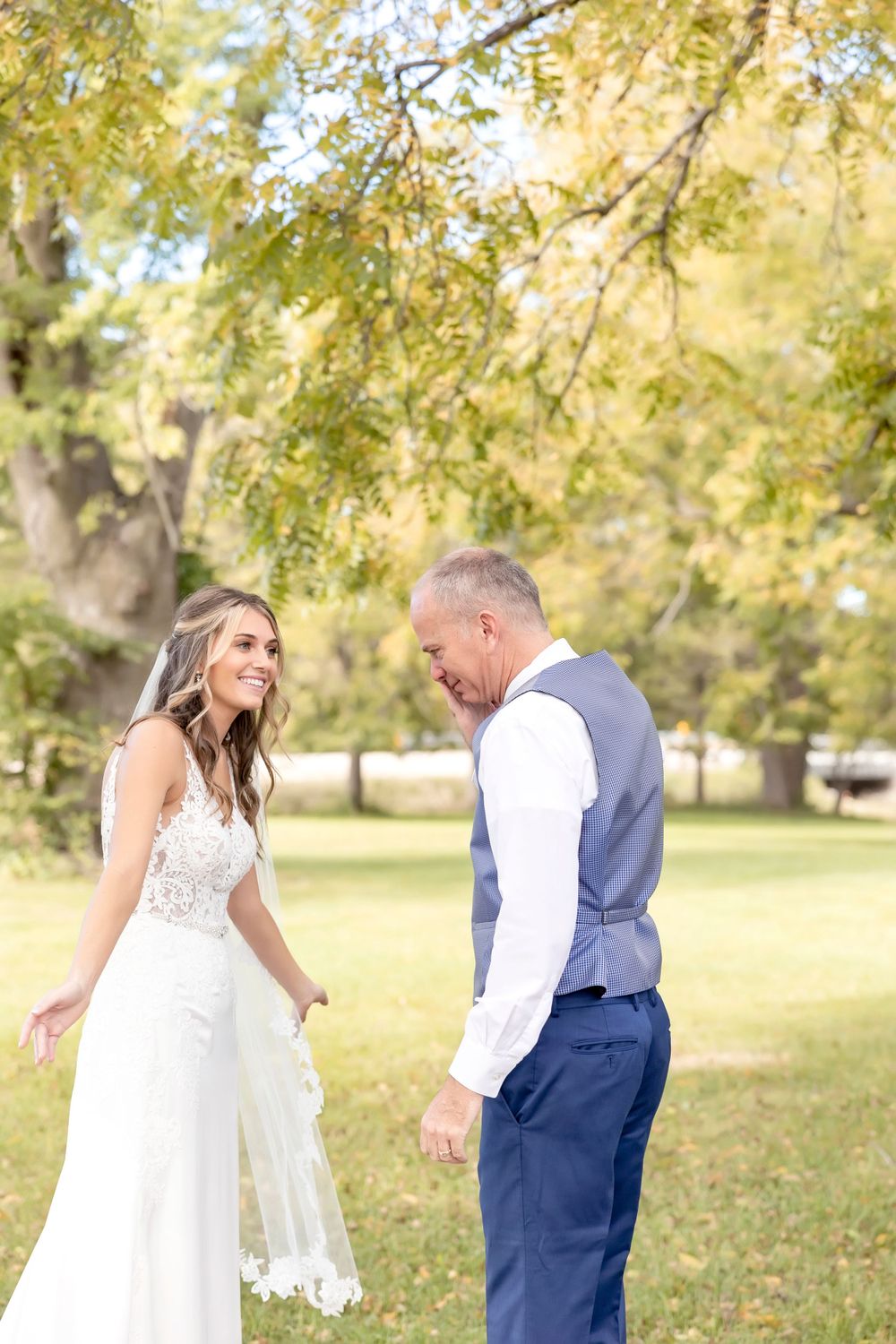 Couple in wedding attire sharing a playful moment in a sunlit park.