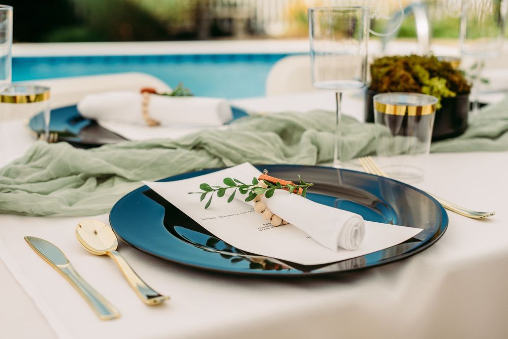 Elegant place setting with blue plates and green accents next to a pool.