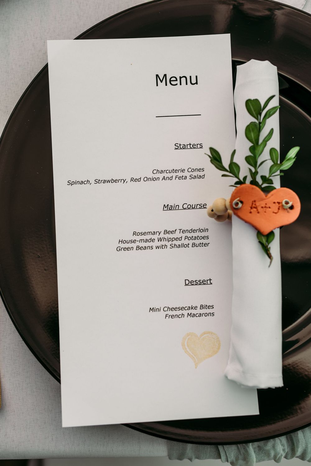 Wedding menu card on dark charger plate with decorative greenery.