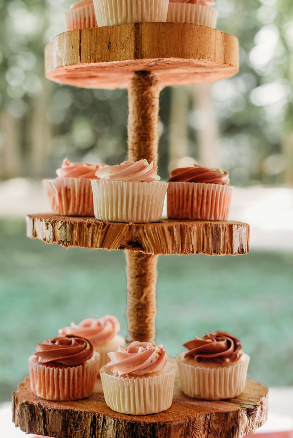Rustic tiered cupcake display with pink and chocolate frosted cupcakes on wooden slices.