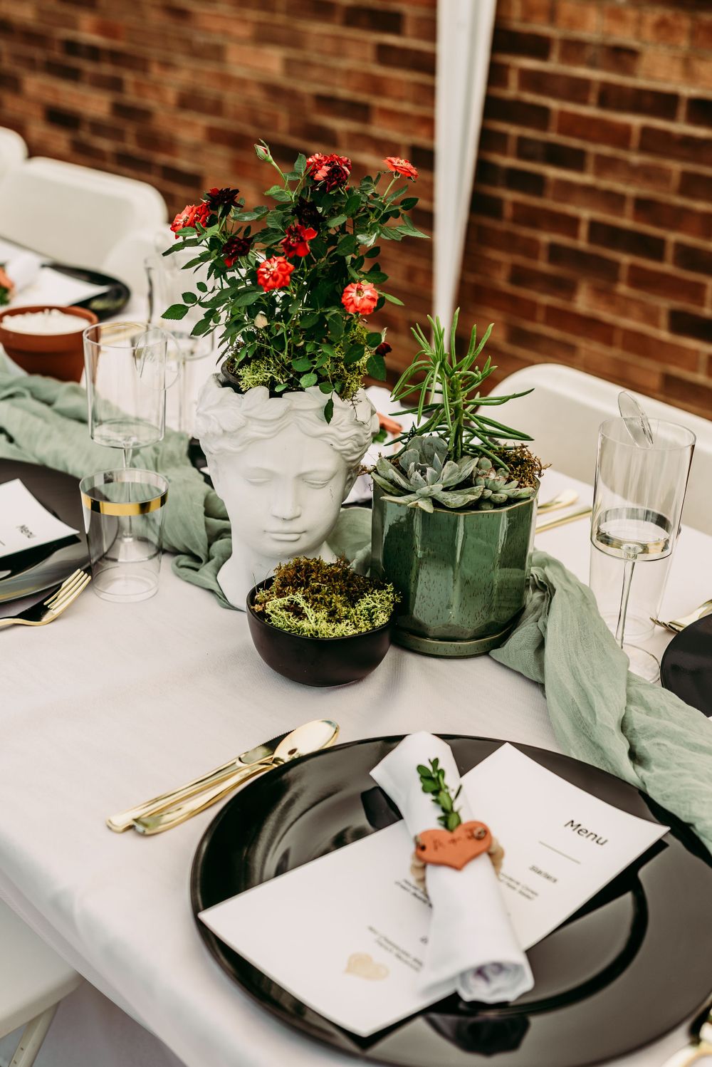 Elegant table setting with white linens, black charger plates and potted centerpieces.