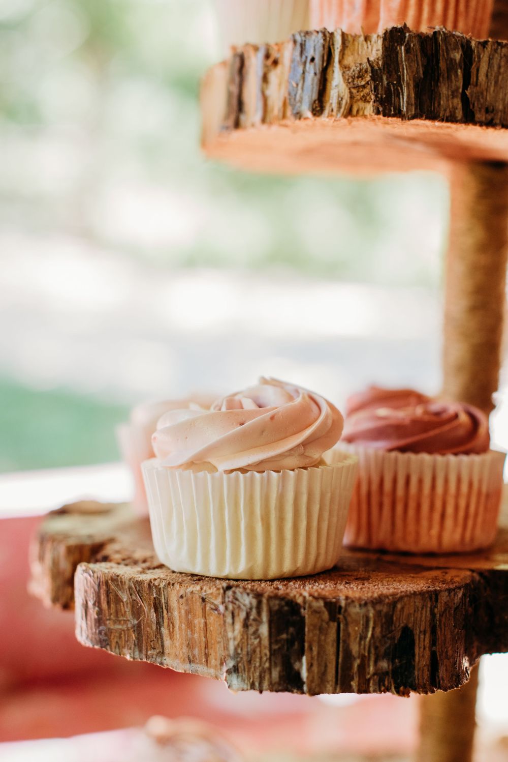 Rustic cupcake display on wooden log slices featuring pink frosted treats.