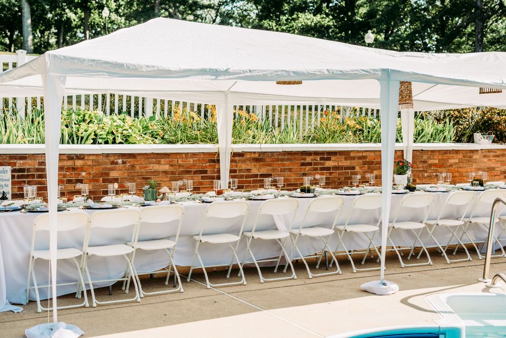 Long rows of white chairs set up outdoors under white canopy tents for an elegant event.