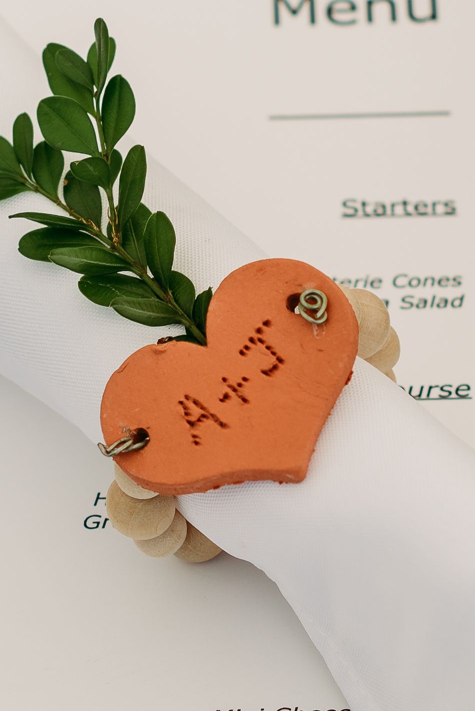 Orange clay heart-shaped place card with delicate writing and green leaves on a white menu.