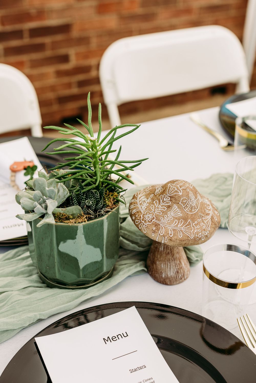 Table setting with succulents in geometric planters, menu cards, and rustic decor on sage green runner.