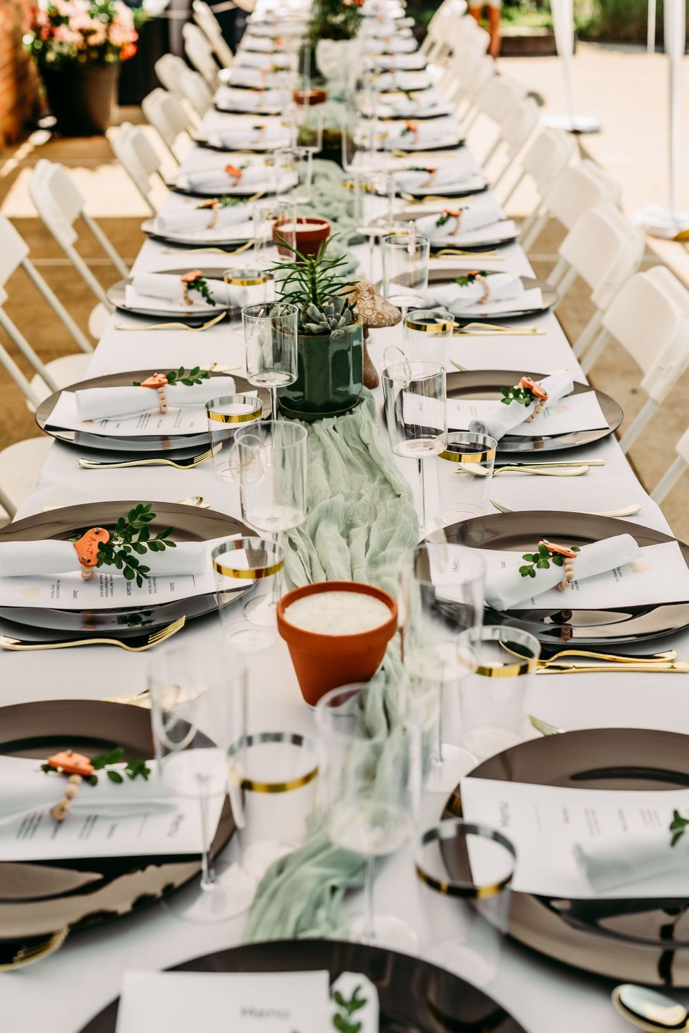 Long dining table set with charger plates and greenery for an elegant event.
