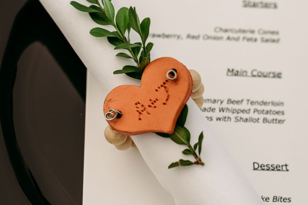 Close-up of a decorative orange heart-shaped name card with greenery against a white menu card.