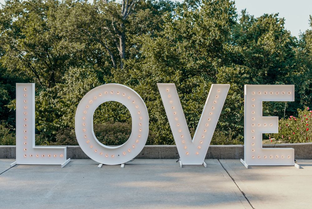 Large white LOVE letters displayed outdoors against a natural tree background.