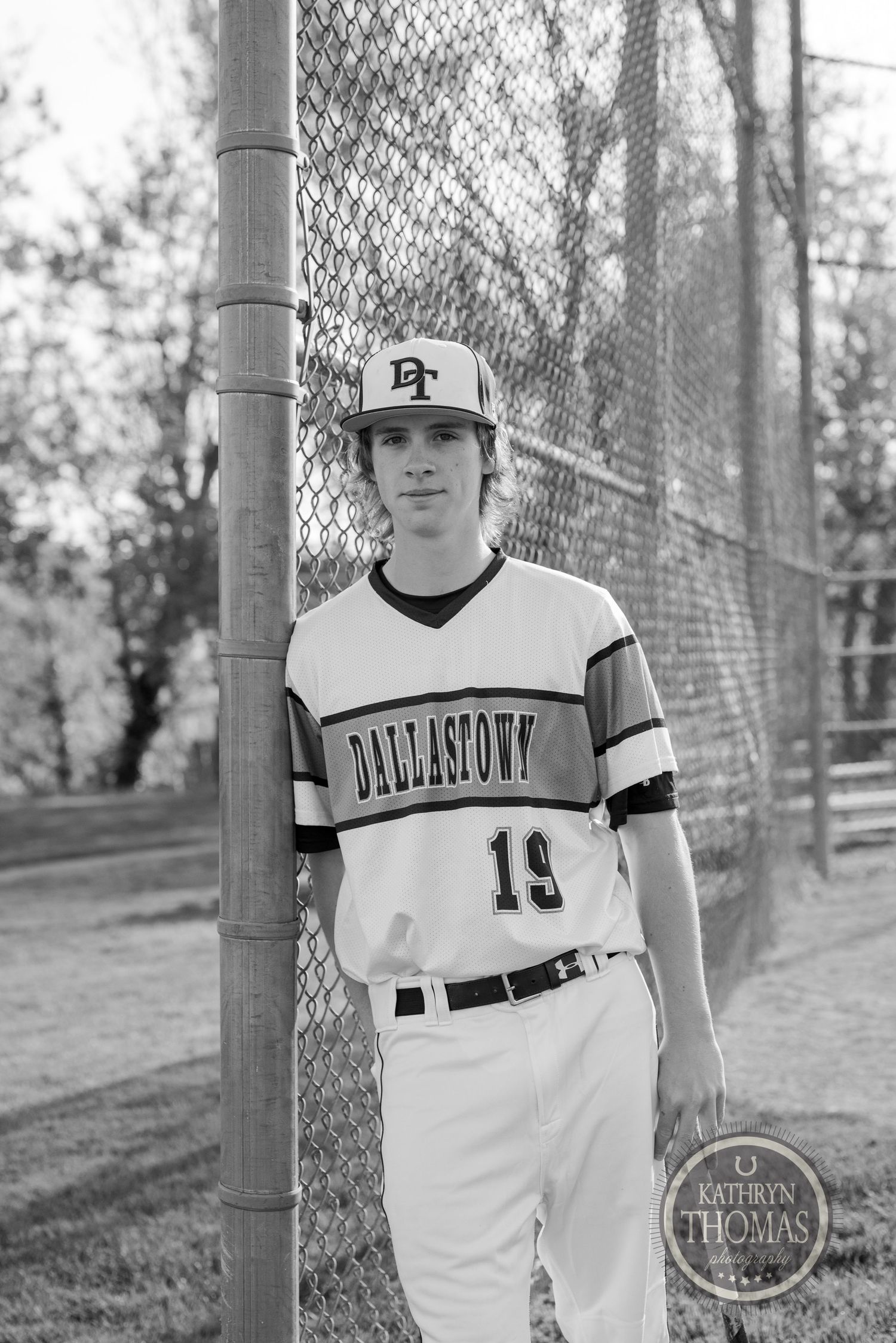 Baseball player in Darlington jersey poses by chain link fence in black and white photo.
