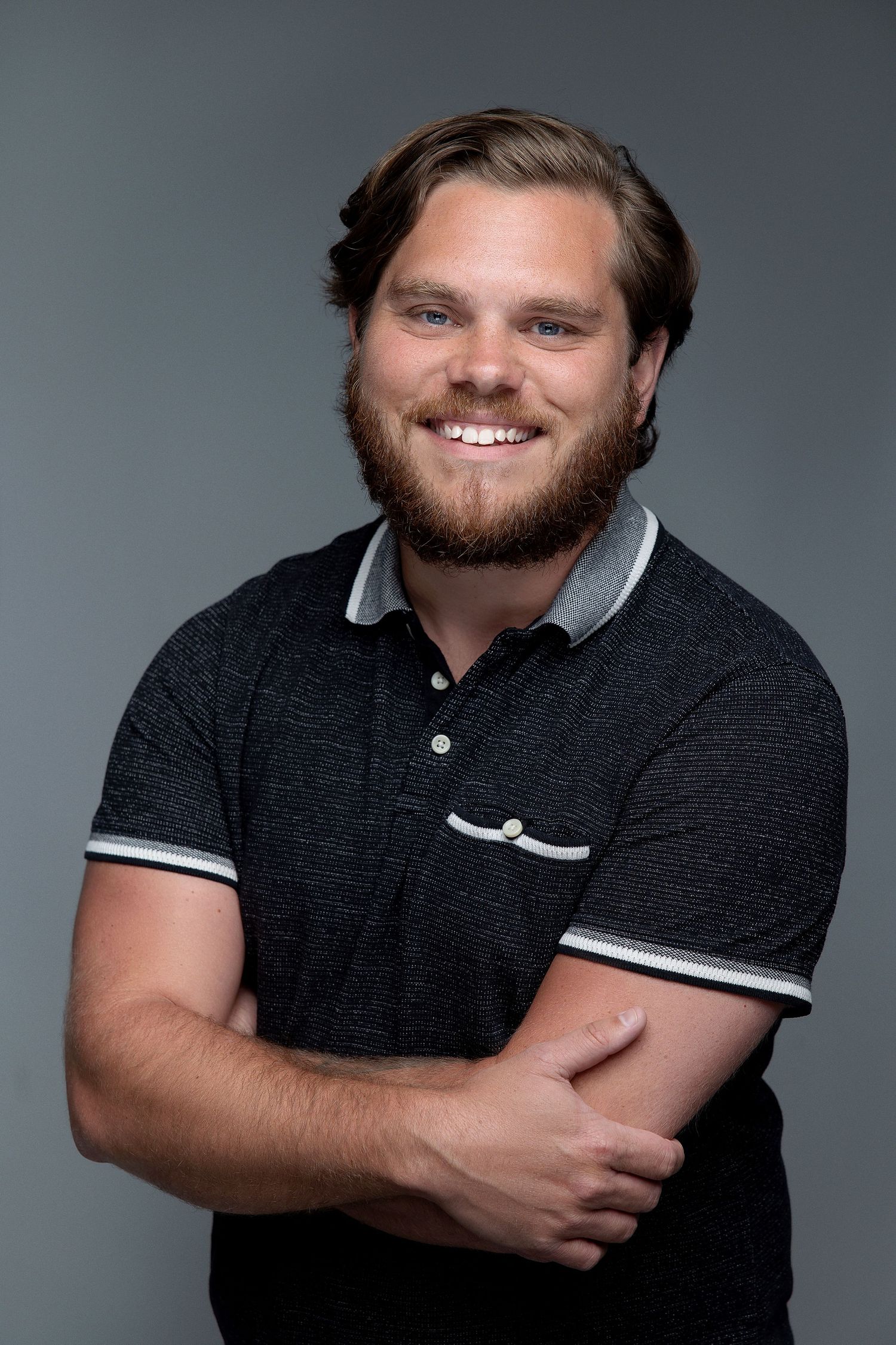 Studio portrait against grey background showing someone in black polo shirt with friendly expression.