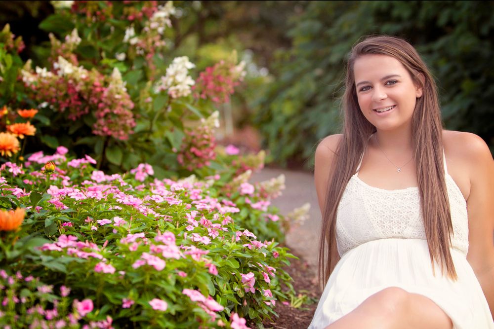 A person in a white dress poses in a colorful garden with pink and orange flowers.