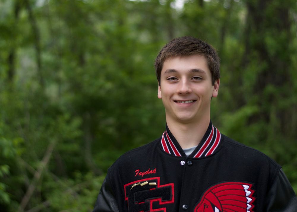 Student in varsity jacket with red and black colors poses outdoors.
