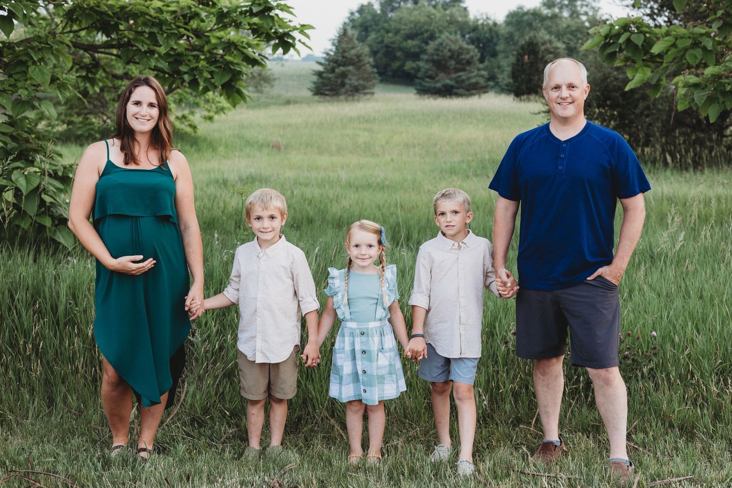 Family portrait in a grassy field with children lined up between parents at sunset.