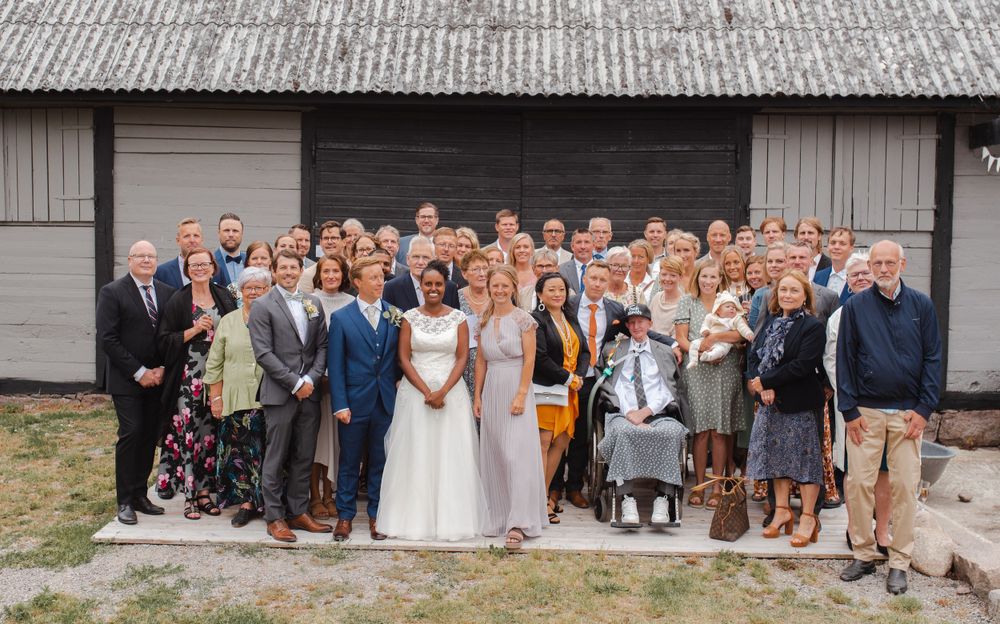 Large wedding party poses for a group photo outside a rustic barn venue.